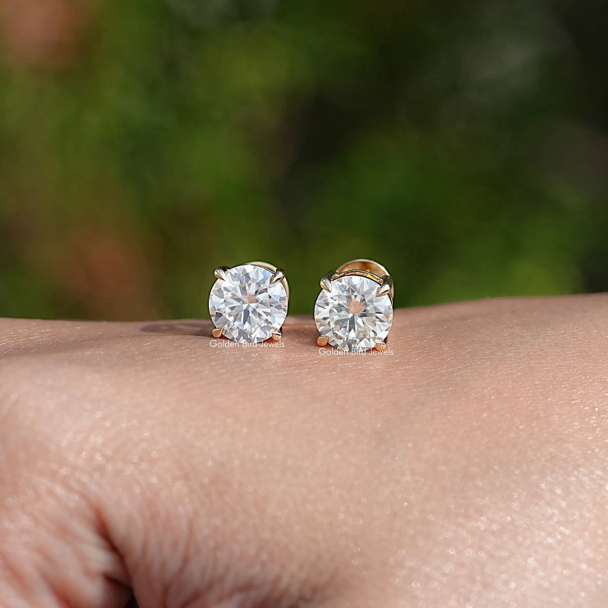 Round moissanite stud earrings with gold-tone setting, pair shown on wrist