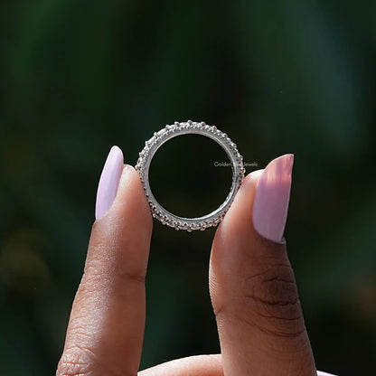 Silver round-stone eternity band ring, front view held between two fingers