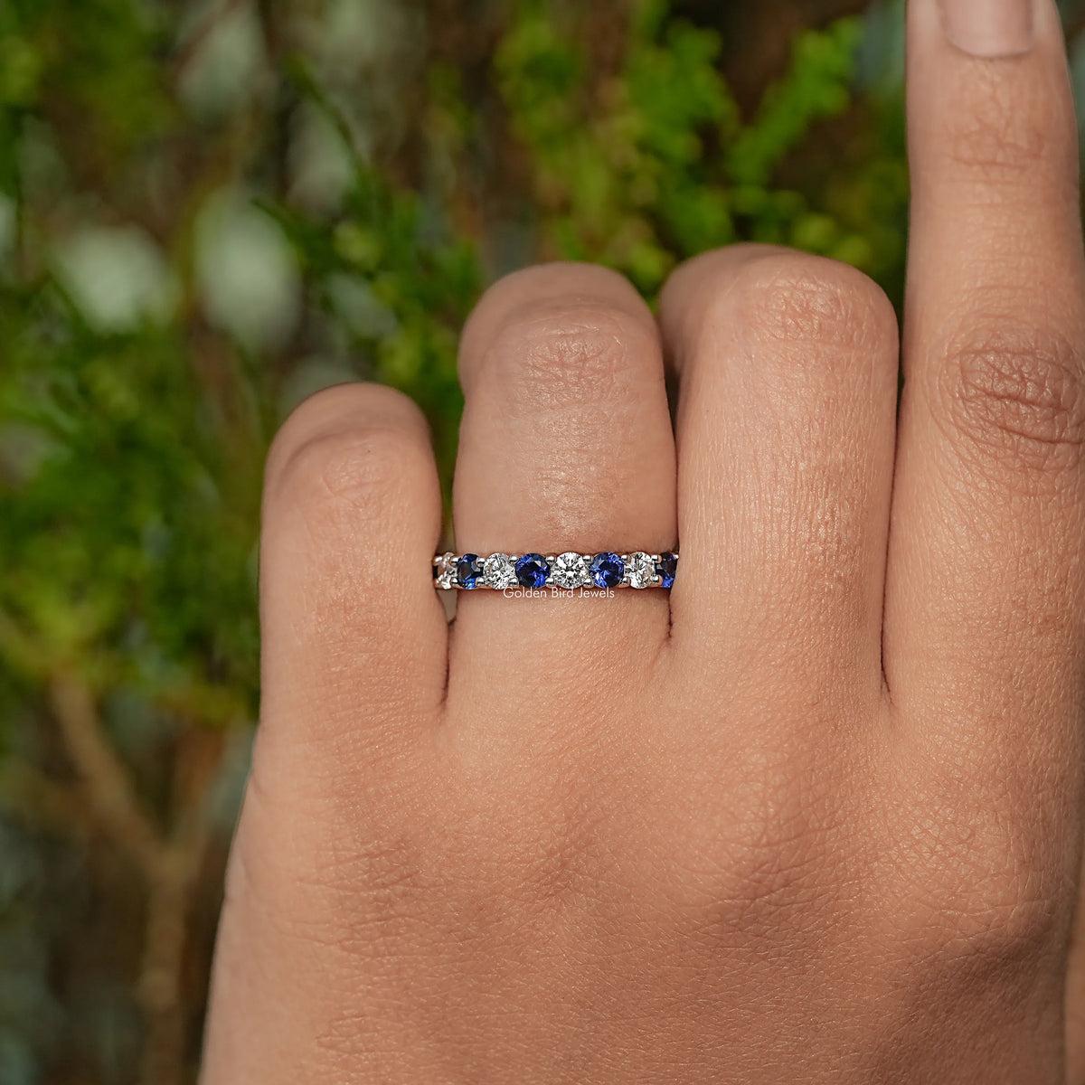 Eternity wedding band on finger with bezel-set round blue gemstones