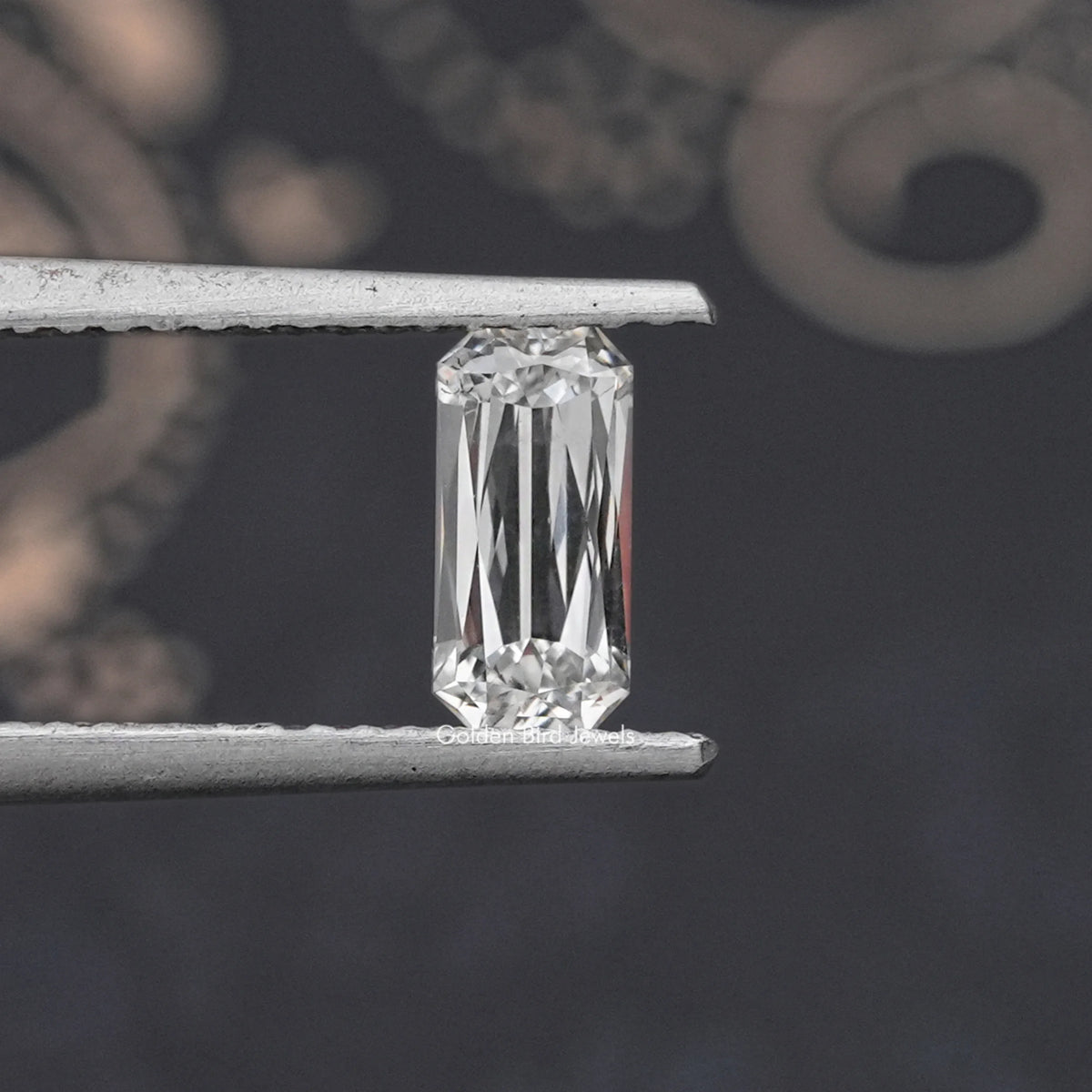 Rectangular lab-grown diamond with scissors-cut facets, held in metal tweezers
