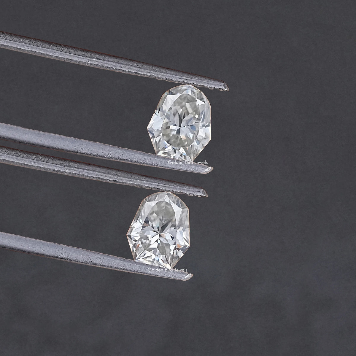 Shield-cut moissanite stones pair in metal prongs, close-up side angle