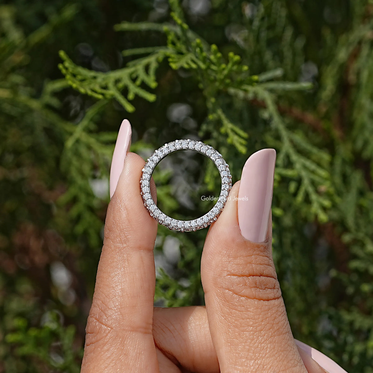 Moissanite eternity band ring with round pavé stones, shown held between fingers