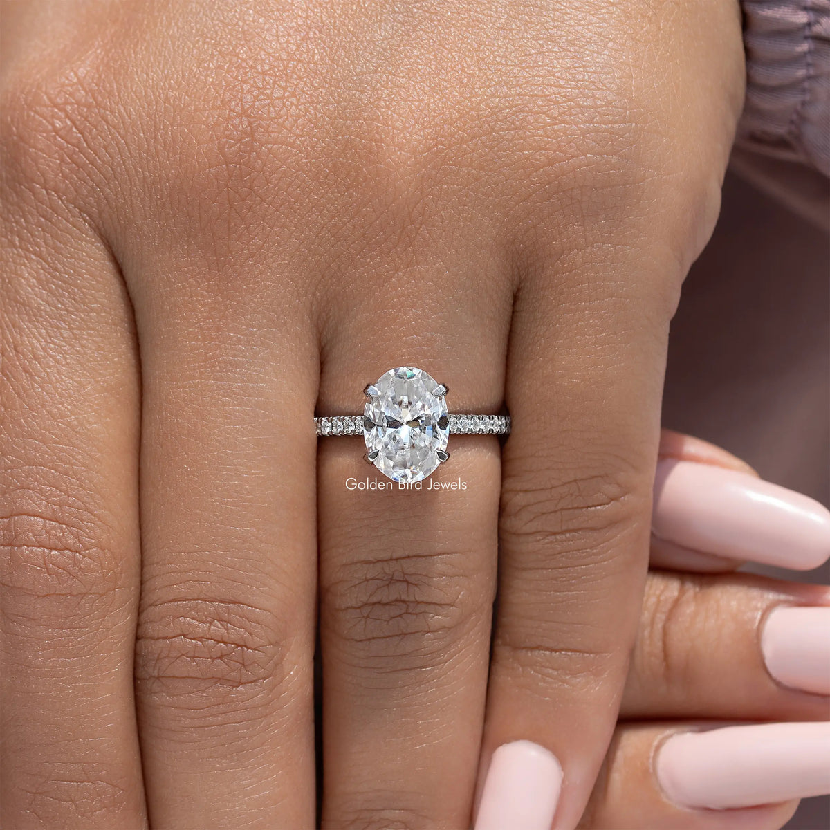 Oval-cut moissanite engagement ring with pave band, held on fingertip