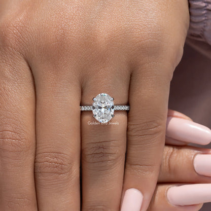 Oval-cut moissanite engagement ring with pave band, held on fingertip