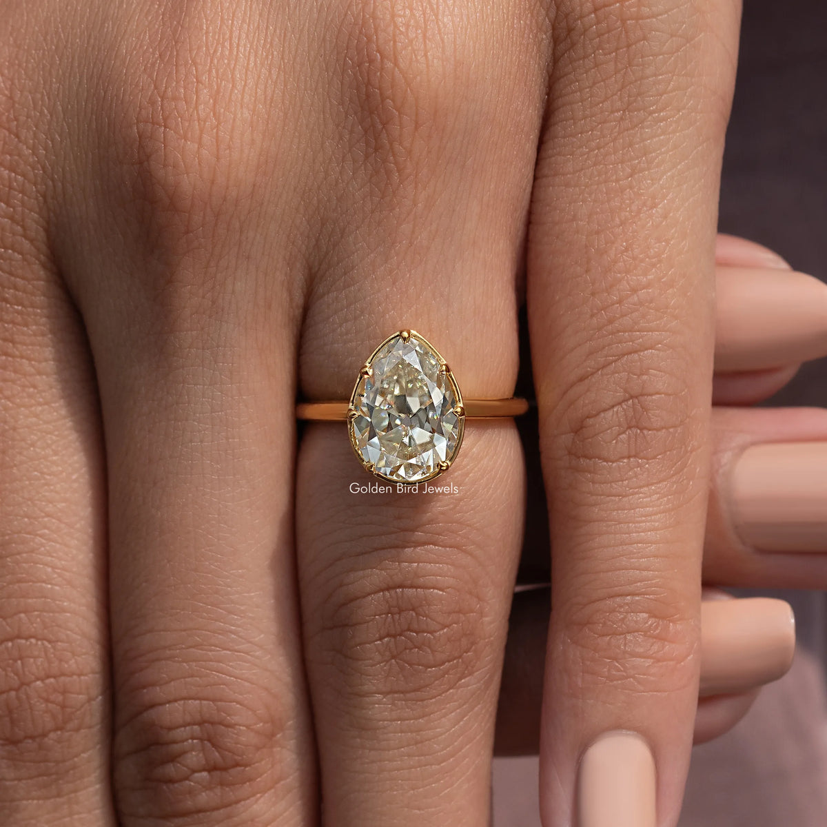 Gold-tone pear moissanite solitaire engagement ring on finger, stone in focus