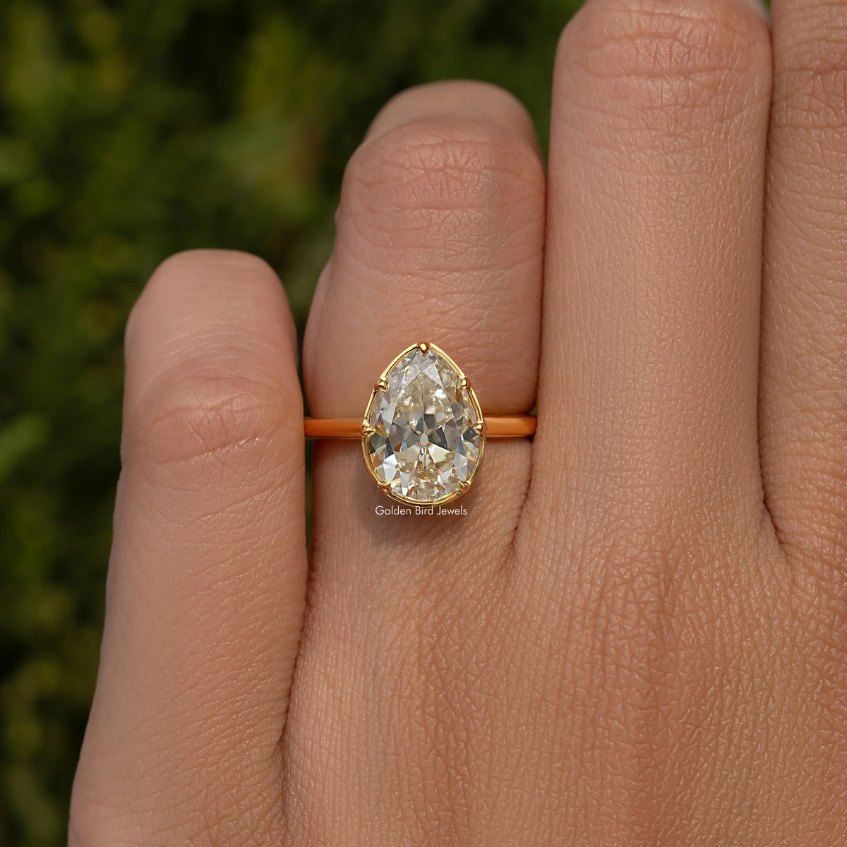 Gold-tone pear moissanite solitaire ring with prongs, close-up on finger