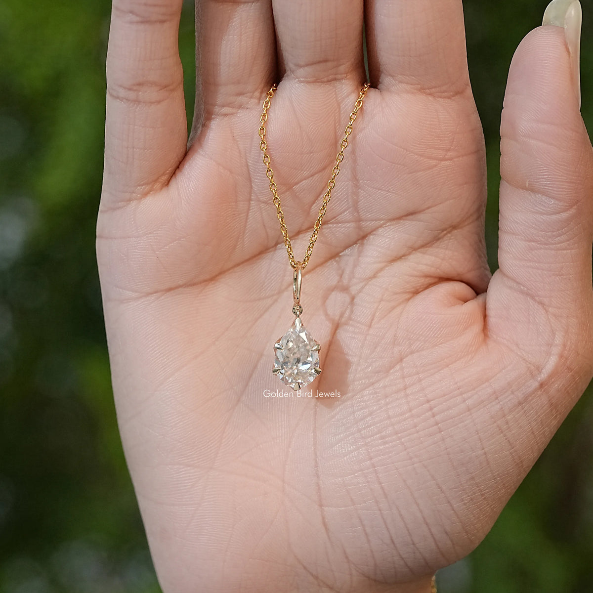Gold-tone chain with pear-cut moissanite teardrop solitaire pendant in palm