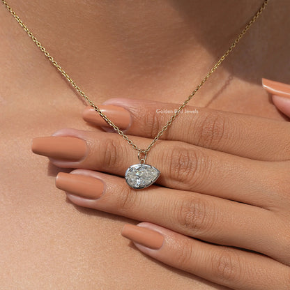 Gold-tone pear-shaped bezel solitaire pendant on chain, close to fingernails