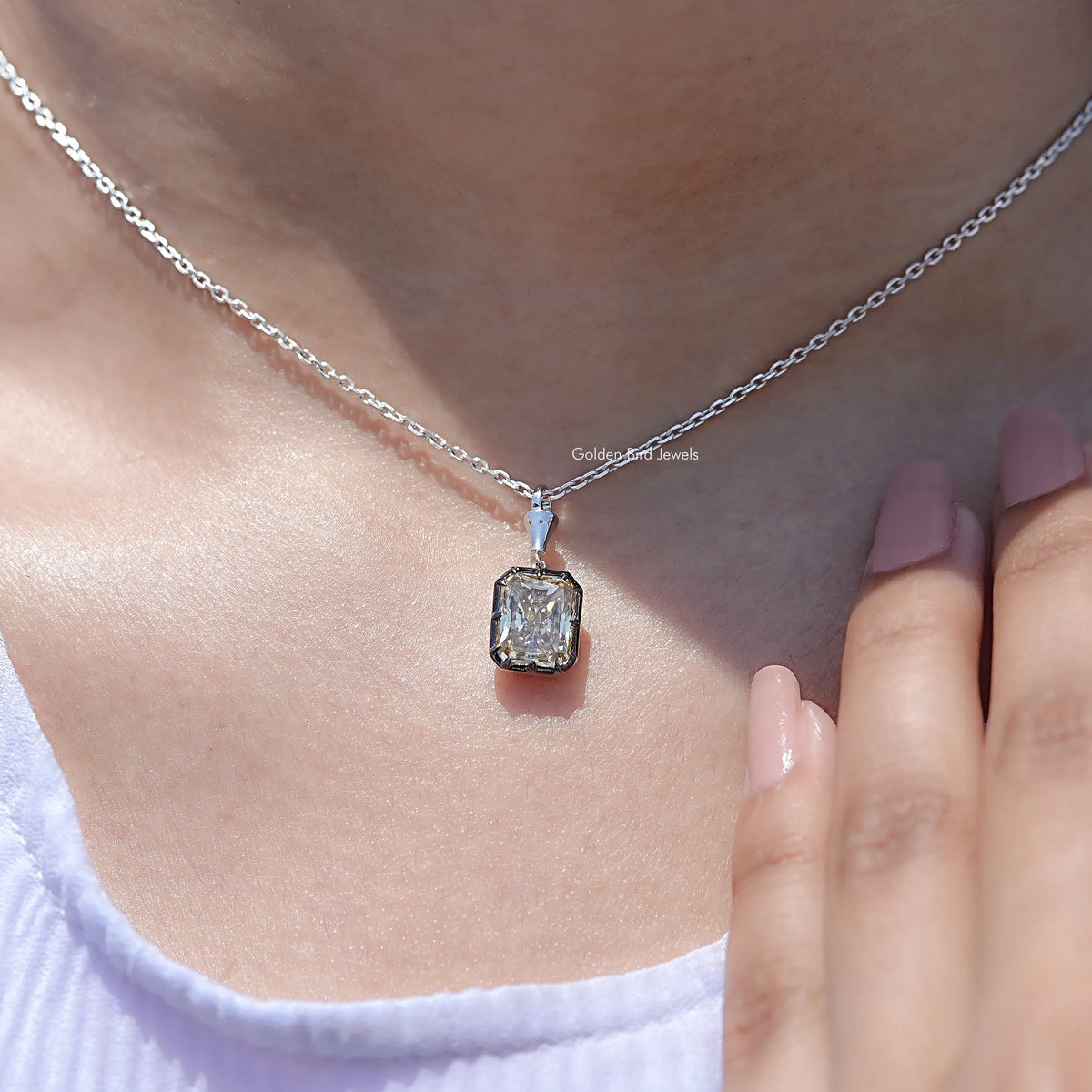 Square-cut moissanite solitaire pendant on silver chain near fingers