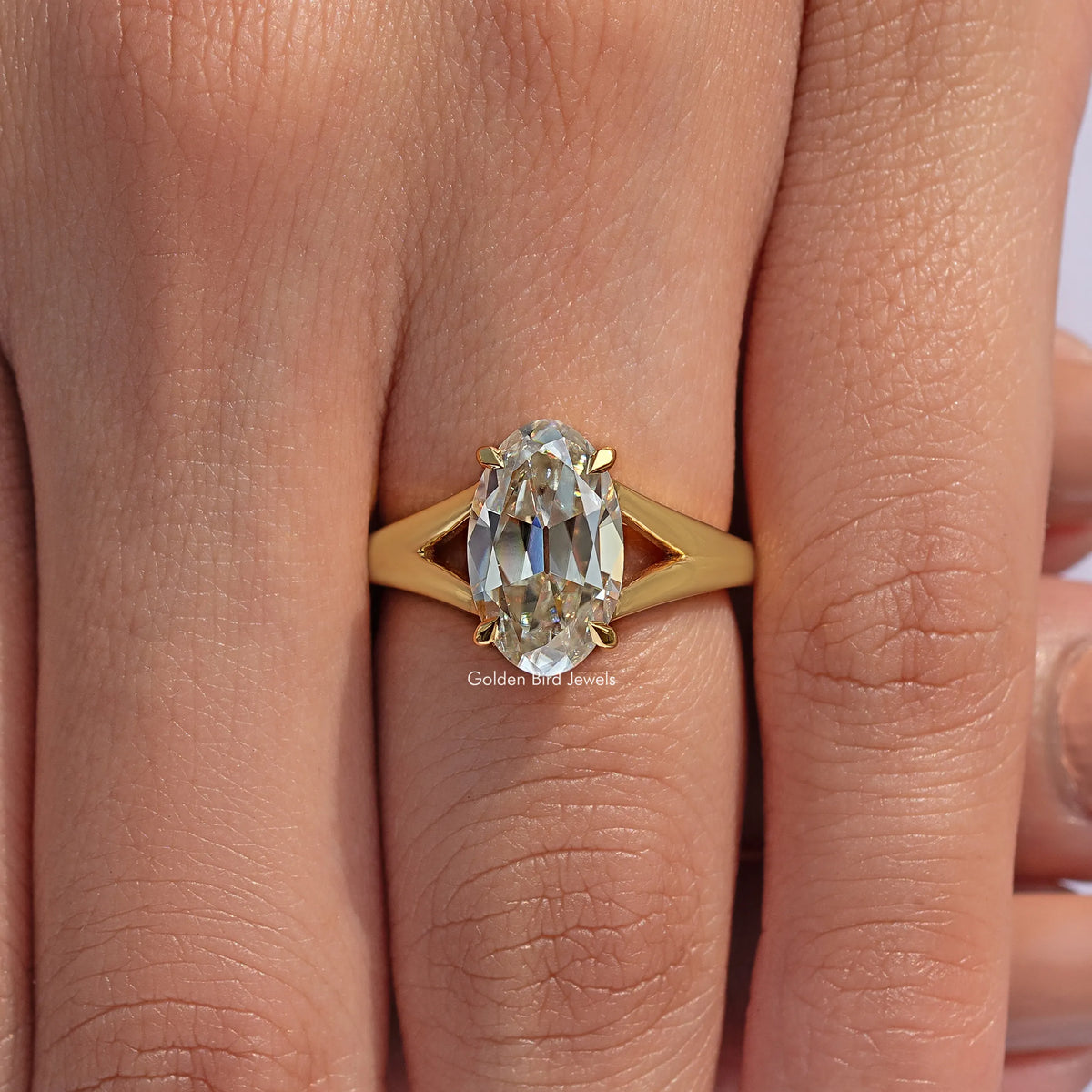 Yellow gold-tone split shank oval moissanite engagement ring on finger