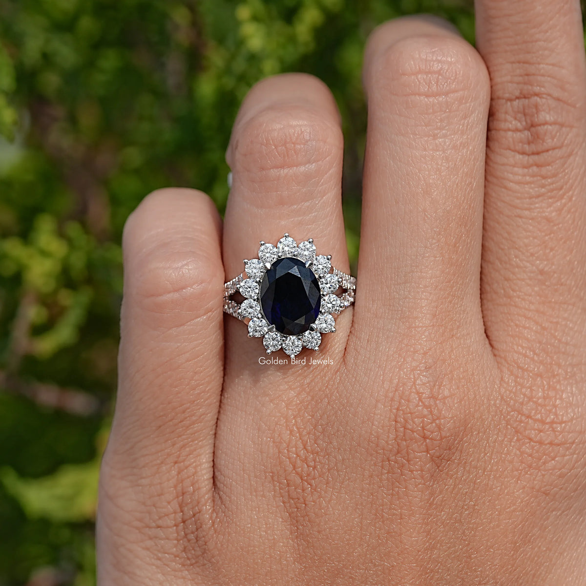 Oval dark sapphire halo ring with split shank and bright side stones
