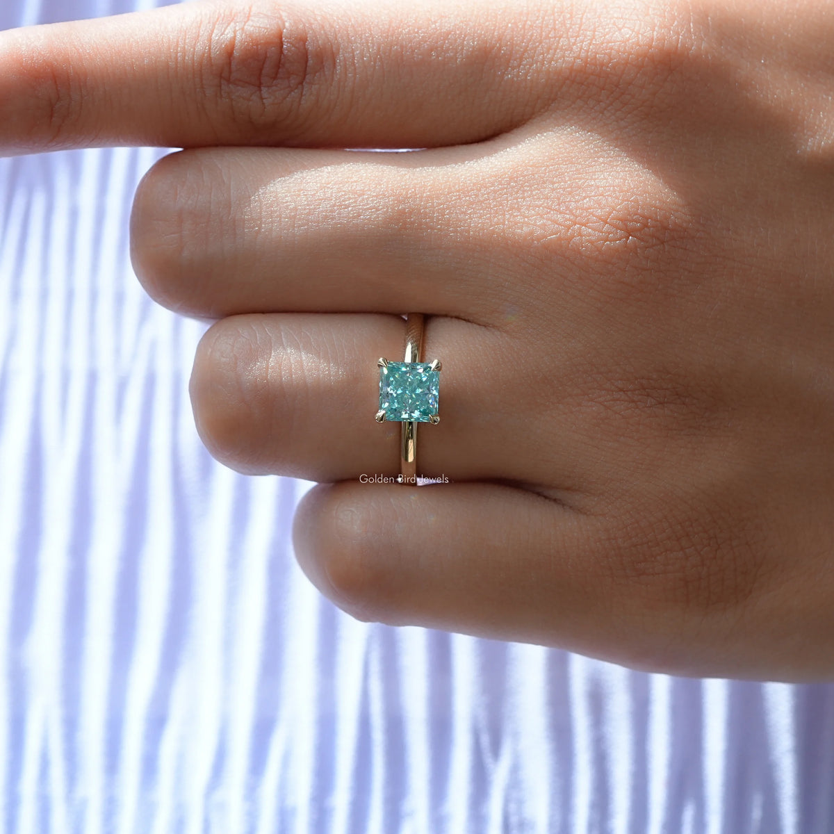 Silver princess-cut solitaire ring with cyan-blue square stone, centered on hand