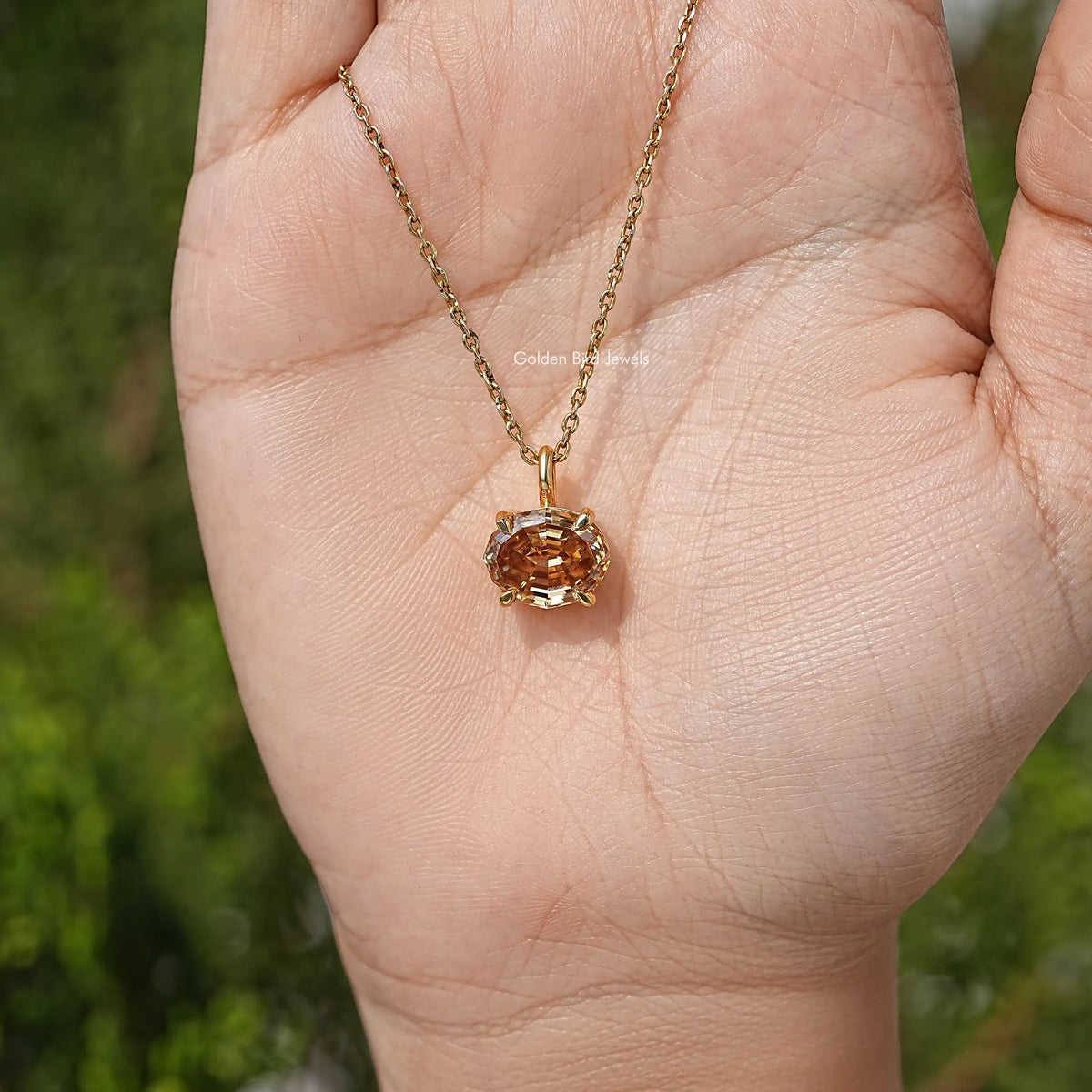 Champagne oval moissanite pendant on gold chain, held in open hand