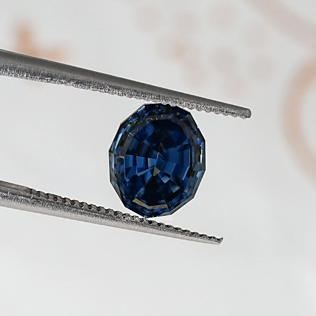 Loose step-cut oval blue moissanite gemstone between metal tweezers