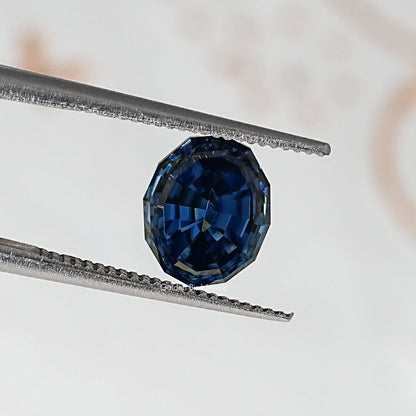 Loose step-cut oval blue moissanite gemstone between metal tweezers