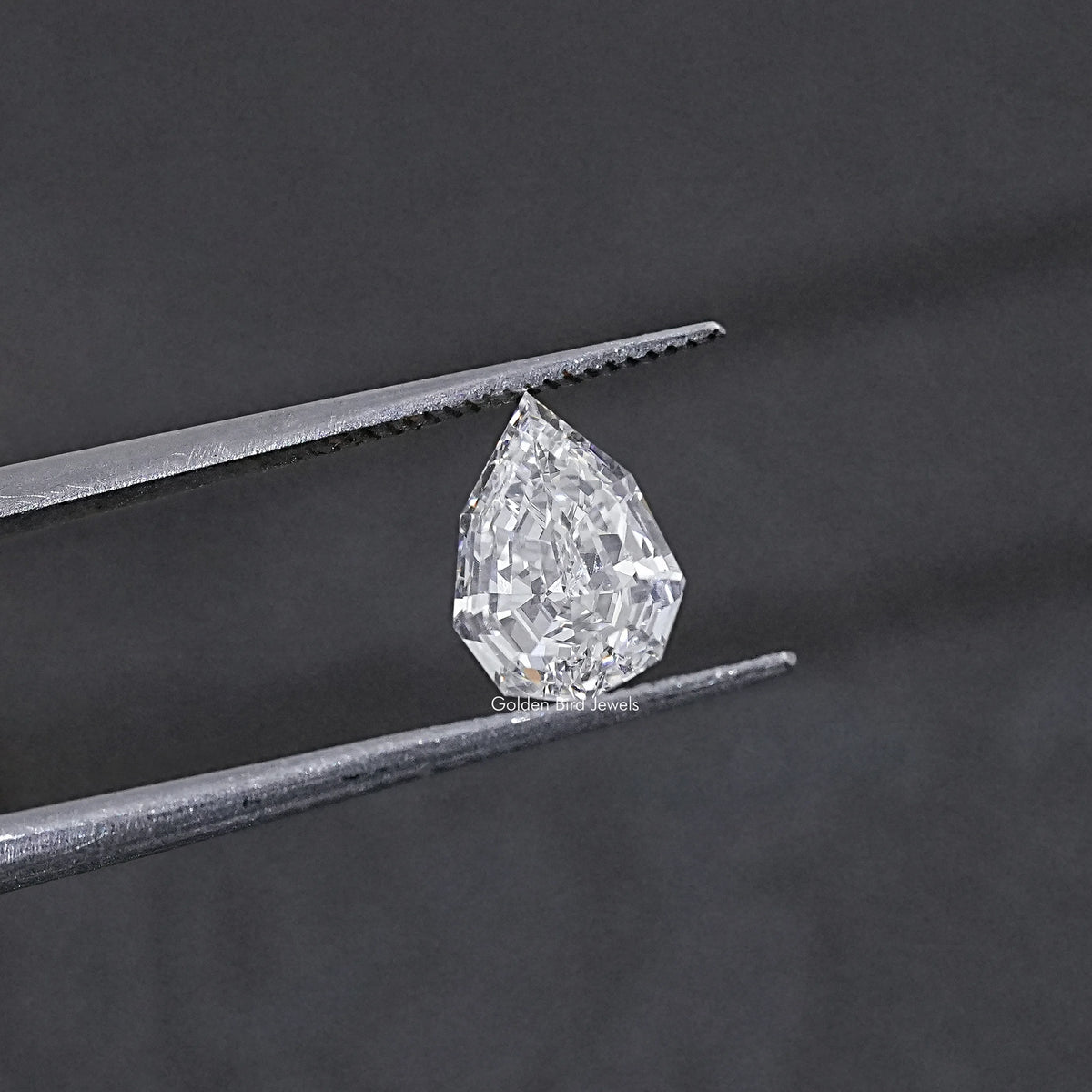 Lab-grown pear-cut diamond held between metal tweezer tips, step-cut facets