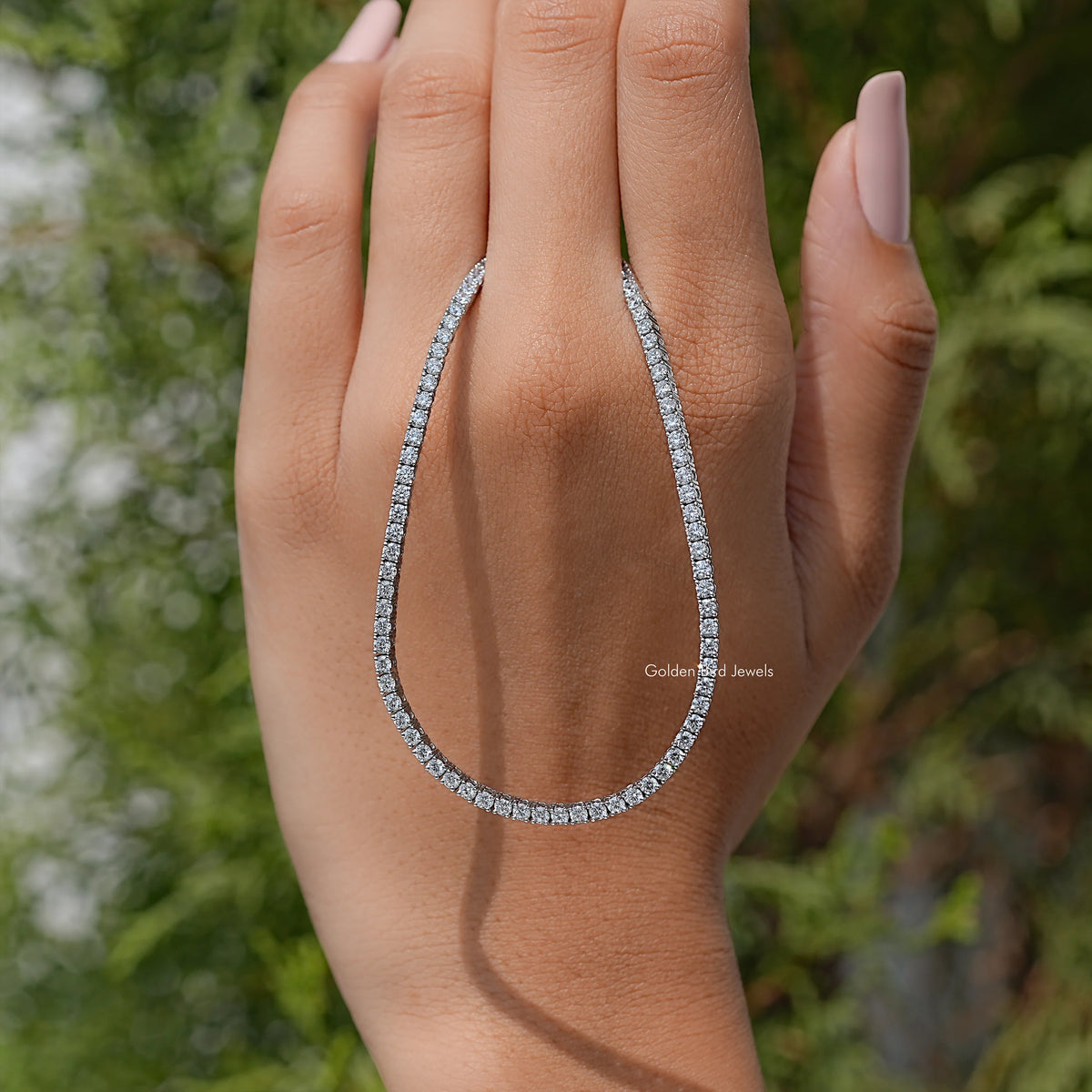 Lab-grown diamond tennis necklace with round-cut stones on open hand, elongated teardrop