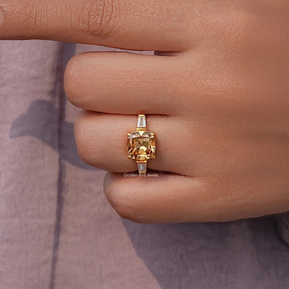 Gold cushion-cut engagement ring with baguette side stones on finger