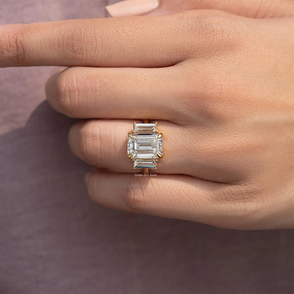 Three-stone emerald-cut moissanite ring side view on finger, gold-tone band and stones.