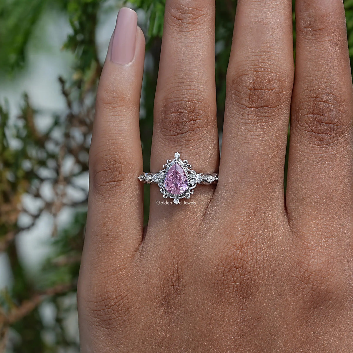 Pink pear-cut gemstone halo ring with ornate setting, worn on hand