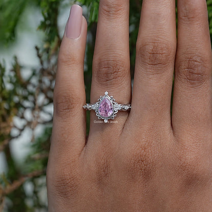 Pink pear-cut gemstone halo ring with ornate setting, worn on hand