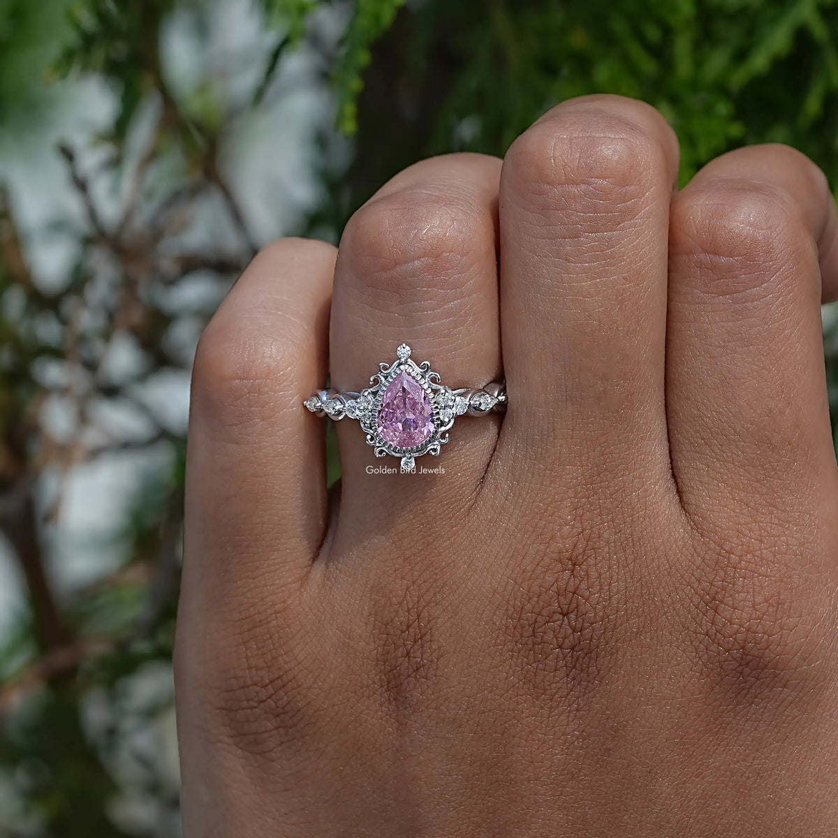 Pink pear-cut gemstone ring with ornate halo and prong-set side stones