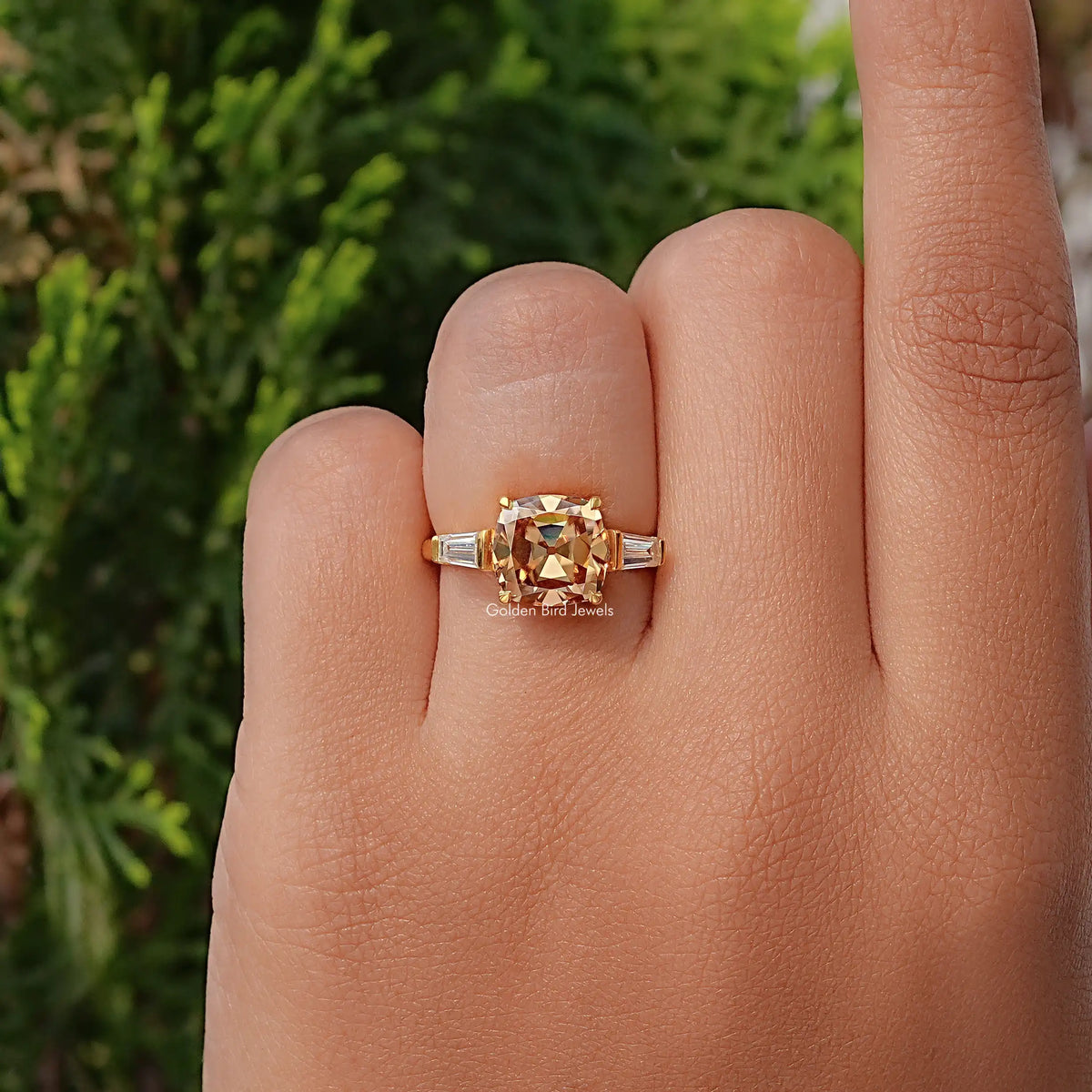 Gold cushion-cut three-stone engagement ring with baguette side stones, worn on finger