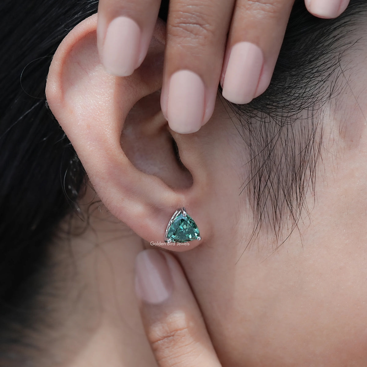 Dark green trillion-cut moissanite stud earrings close-up on ear