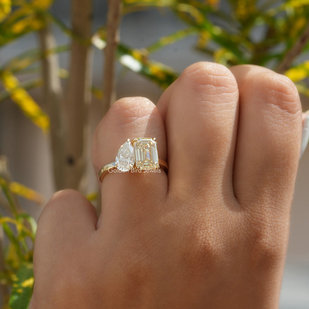 Two-stone toi et moi ring on finger with gold-toned band and prong-set center stone