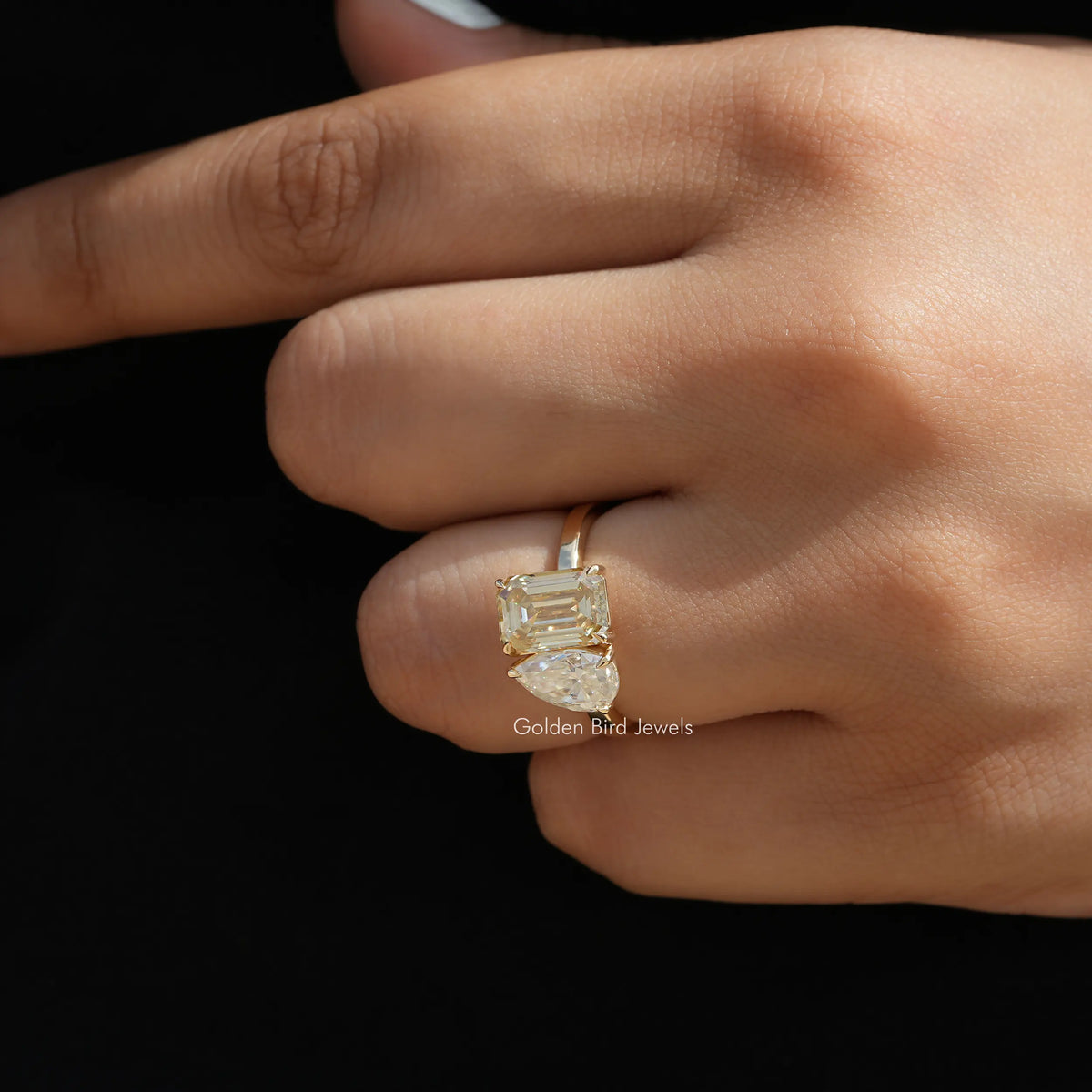 Gold-toned toi et moi ring with a prong-set emerald-cut stone on finger