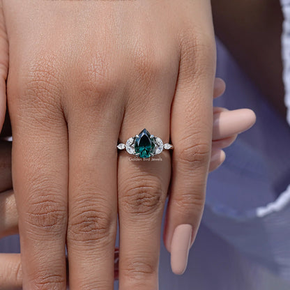 Green pear-cut moissanite engagement ring on hand with round halo and side stones