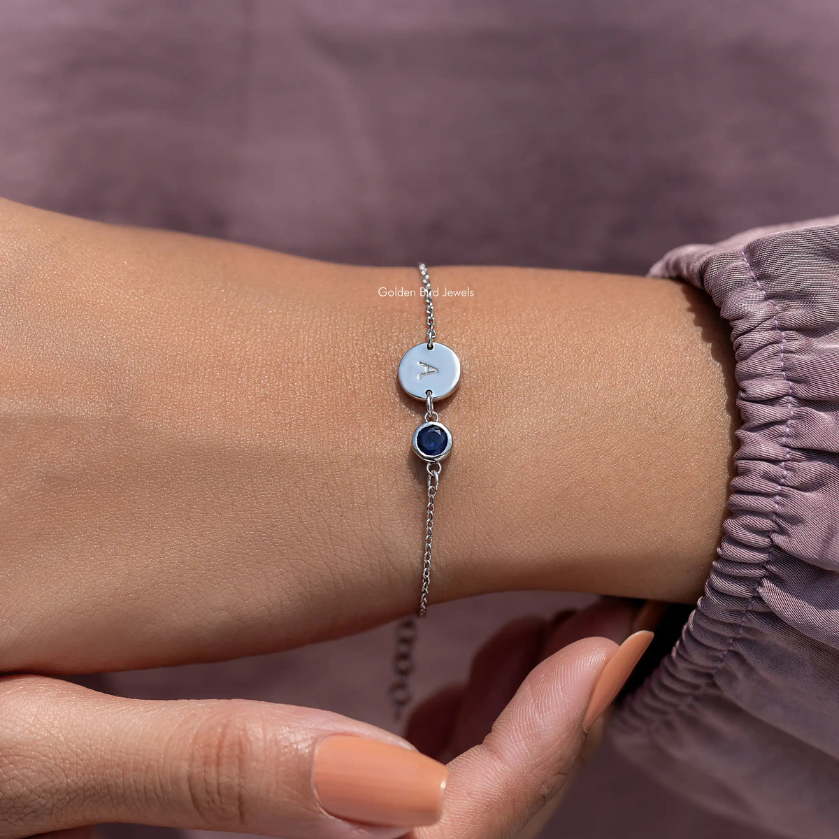 Close view of sterling silver bracelet with light blue initial A disc and dark blue gem