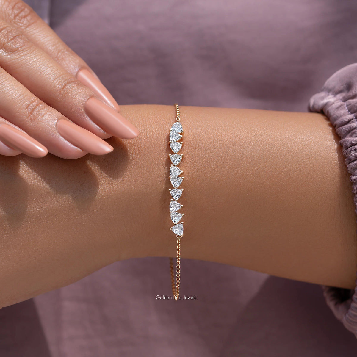 Gold diamond line bracelet with marquise-cut stones worn on wrist, fingers nearby