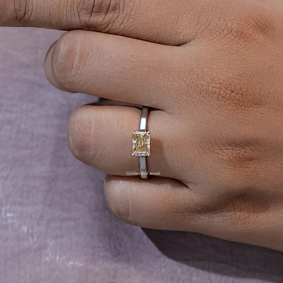 Yellow emerald-cut solitaire ring on silver-tone band, close-up on finger