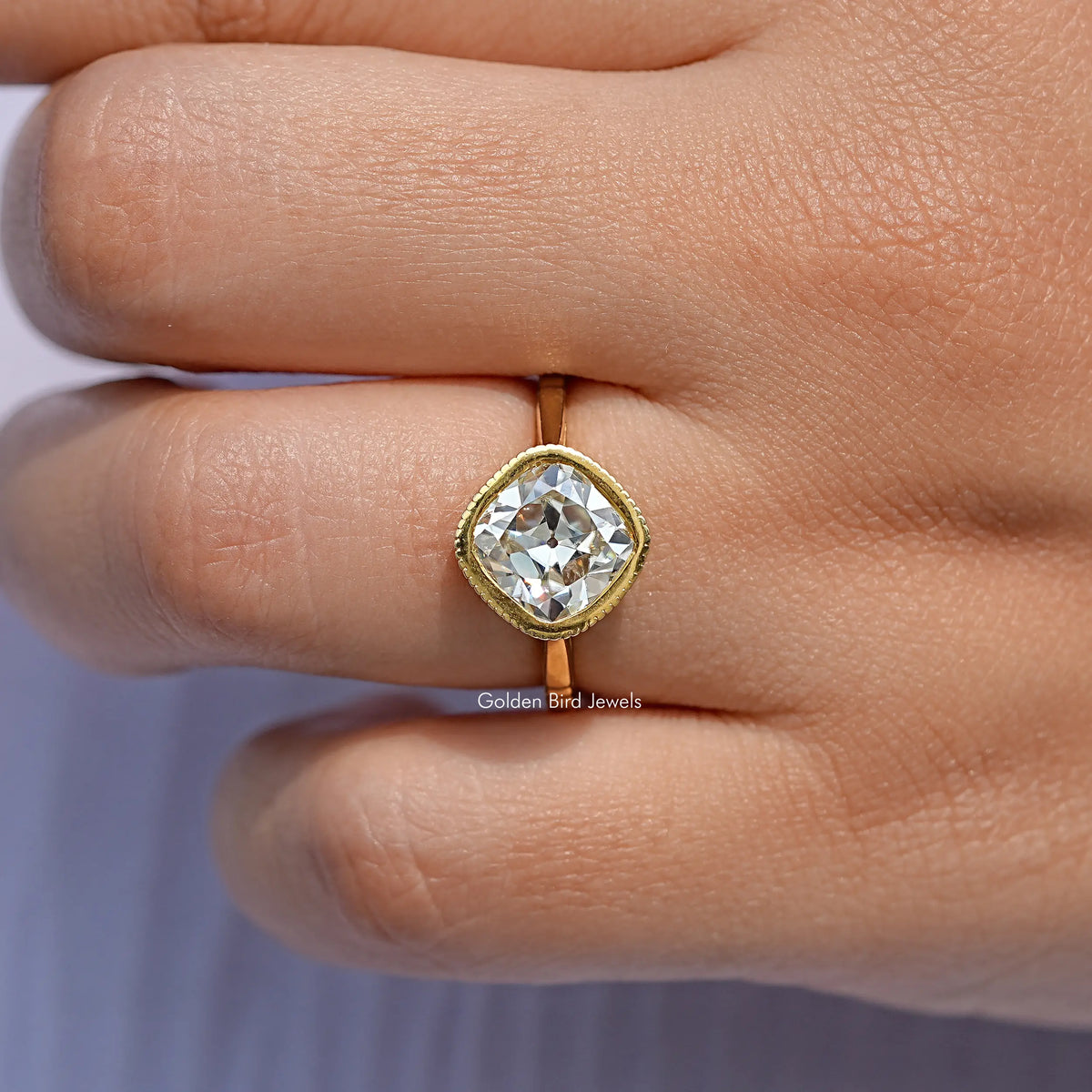 Gold cushion-cut solitaire ring on finger, rounded bezel setting