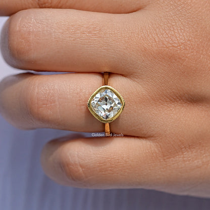 Gold cushion-cut solitaire ring on finger, rounded bezel setting