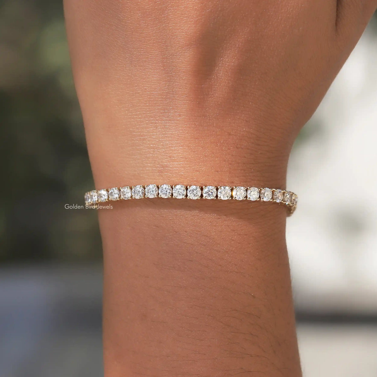 Moissanite tennis bracelet featuring round-cut stones, gold-tone, on bare wrist