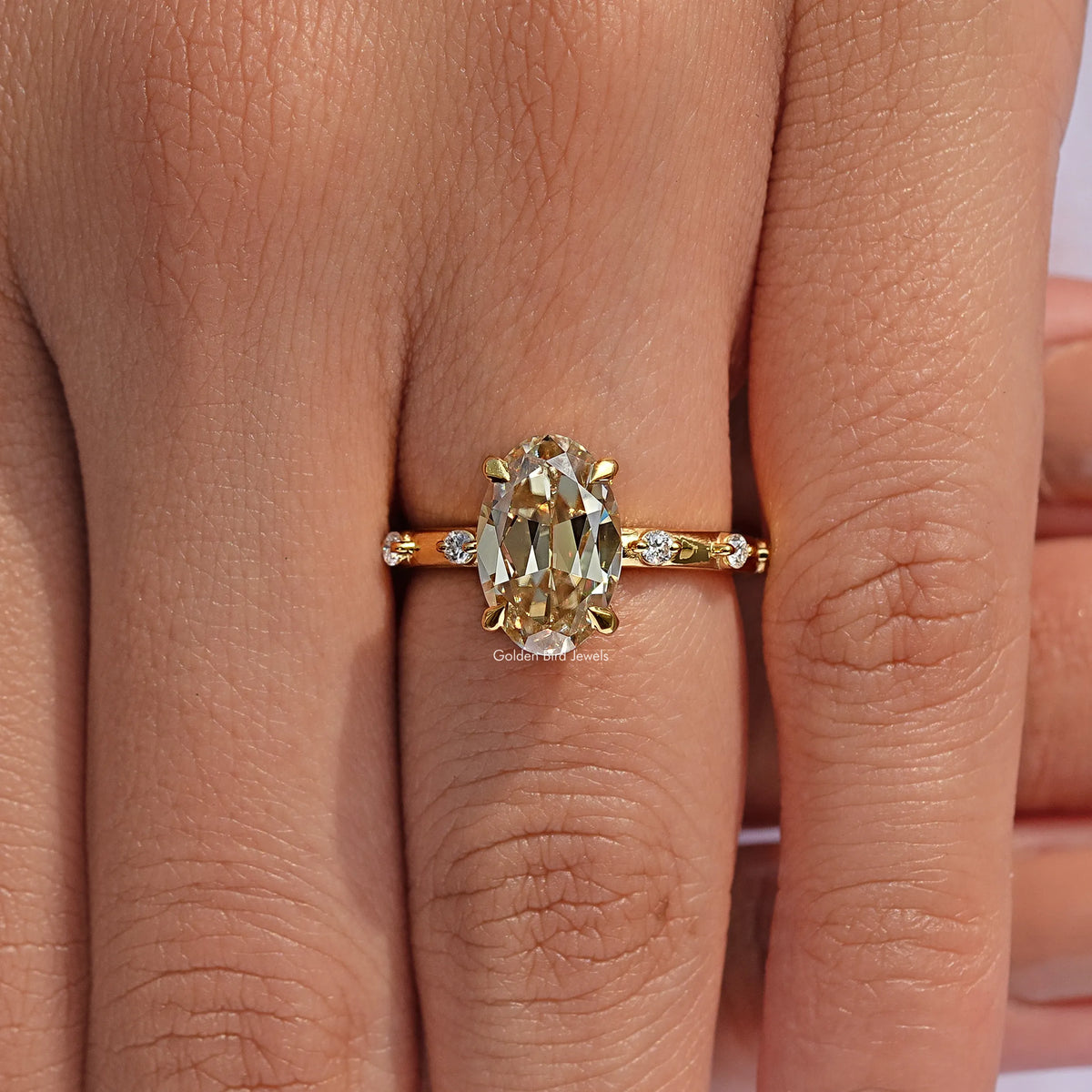 Gold-tone oval-cut center stone engagement ring on finger, close-up