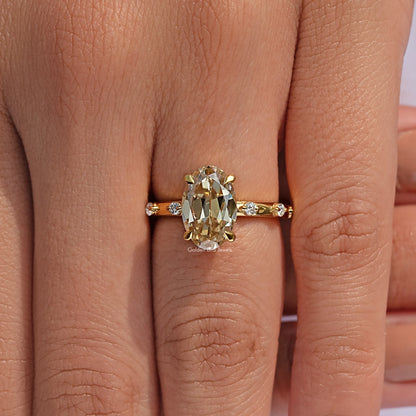 Gold-tone oval-cut center stone engagement ring on finger, close-up