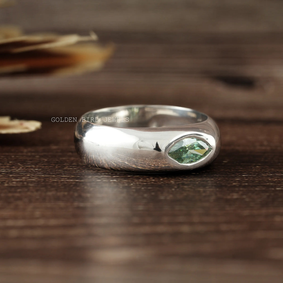 Silver flush-set solitaire ring featuring a green marquise-cut stone on top.