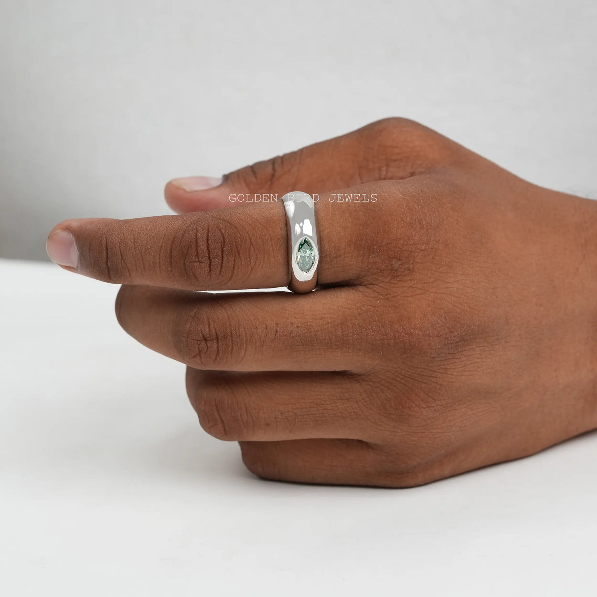 Silver engagement ring on hand with a green marquise-cut solitaire stone.