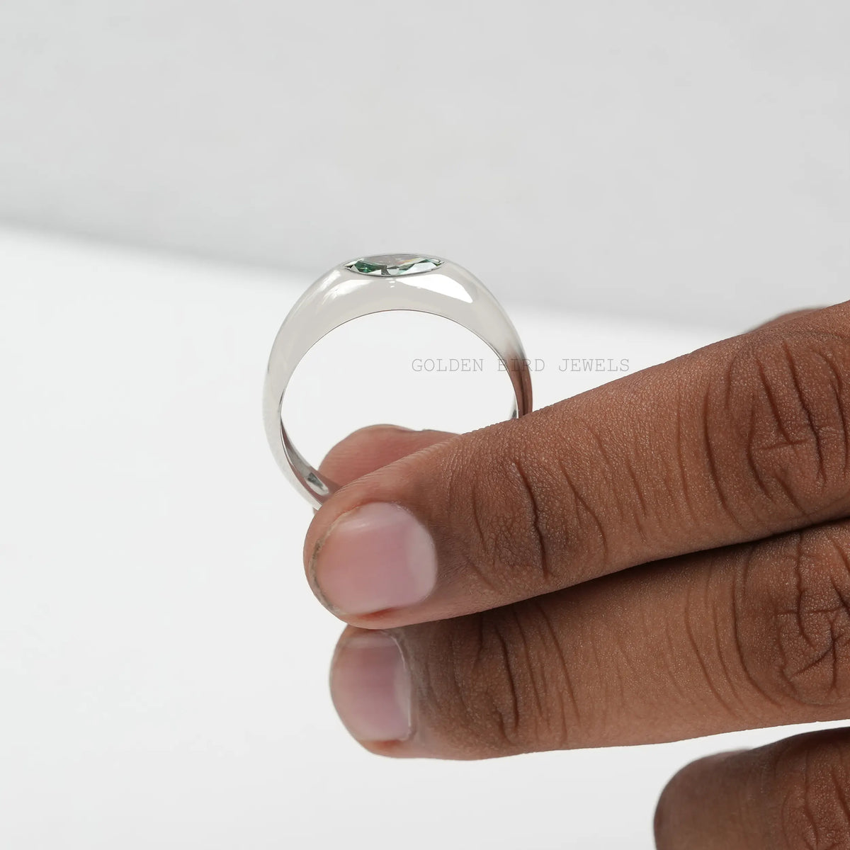 Close-up of silver ring band with green marquise-cut stone, worn on hand.